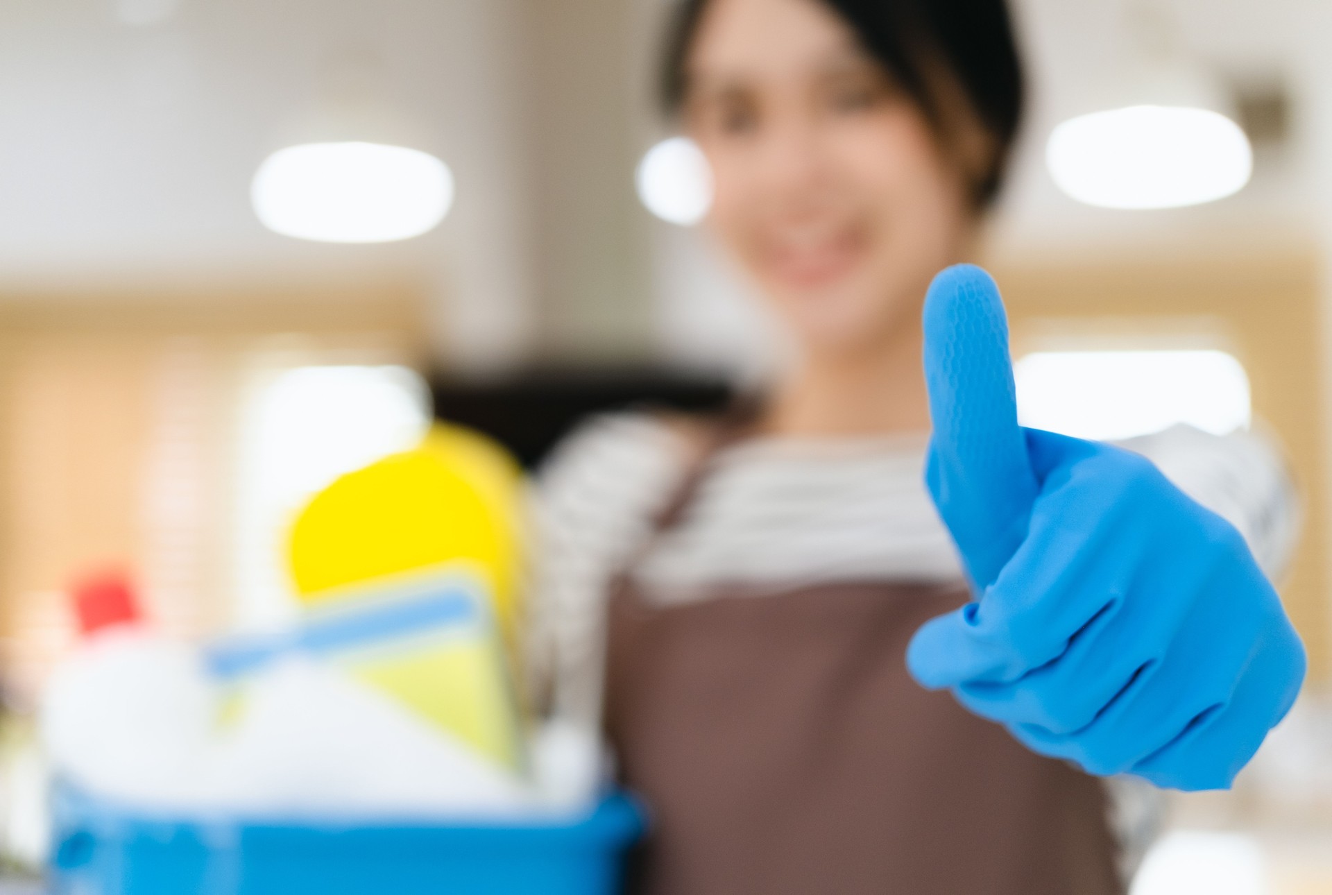 asian woman wearing apron holding cleaning products smiling happy and positive, thumb up doing excellent and approval sign